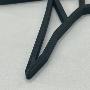 May include: Close-up of a black, 3D printed, geometric star shape. The star has a sharp point and is made of multiple layers of plastic.