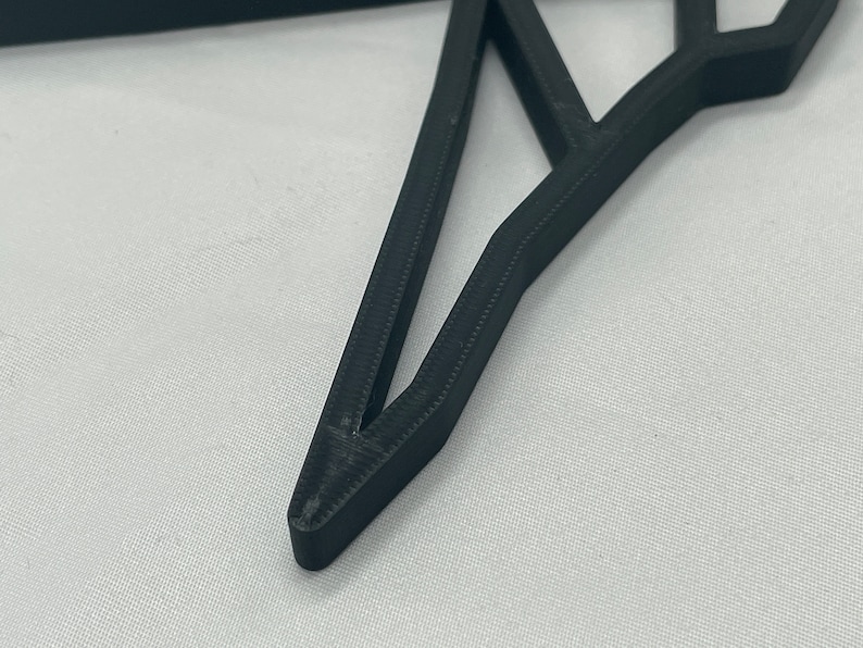 May include: Close-up of a black, 3D printed, geometric star shape. The star has a sharp point and is made of multiple layers of plastic.