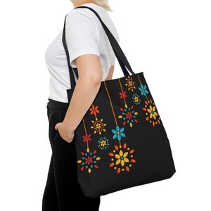 Puede incluir: Una bolsa de tela negra con un diseño floral colorido. Las flores son rojas, naranjas, amarillas, azules y verdes. La bolsa tiene una correa negra.
