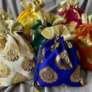 Könnte beinhalten: Eine Sammlung farbenfroher Geschenkbeutel mit Kordelzug in verschiedenen Farbtönen, darunter Weiß, Gelb, Grün, Blau, Orange, Pink und Rot. Jeder Beutel ist mit einem goldenen Paisley-Muster und einem goldenen Bandverschluss verziert.