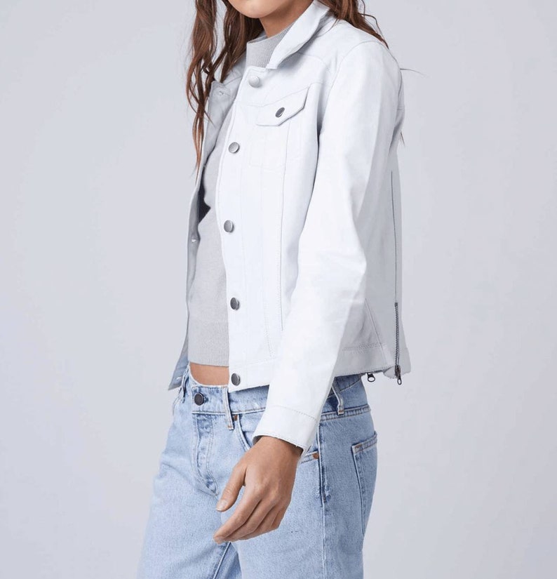 May include: A white denim jacket with a zipper on the side and a button closure. The jacket has a pocket on the left chest.