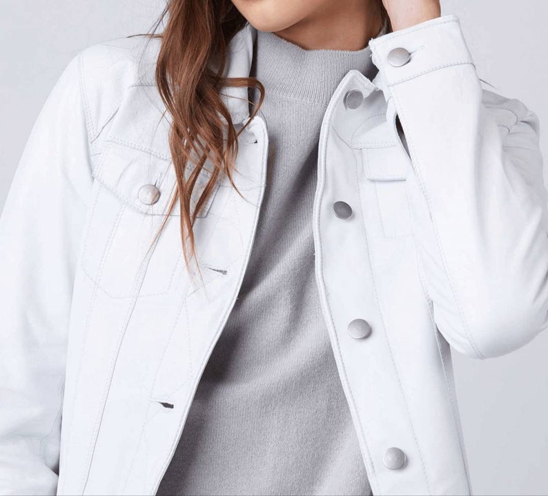 May include: A white leather jacket with silver buttons. The jacket has a classic denim style with a pointed collar and flap pockets.