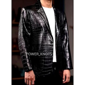 May include: Black leather blazer with a crocodile skin texture. The blazer has a notched lapel, a single-button closure, and a classic tailored fit. The text "POWER_KNOTS" is visible on the front of the blazer.