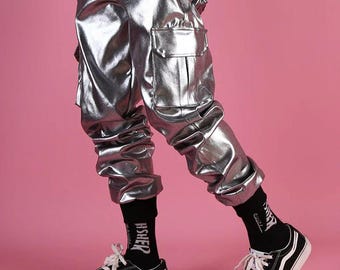 May include: Silver metallic cargo pants with a loose fit and multiple pockets. The pants are worn with black socks and black sneakers.