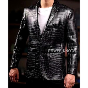 May include: A black leather blazer with a crocodile skin texture. The blazer has a notched lapel, two front pockets, and a single-button closure. The text "POWER KNOTS" is visible on the front of the blazer.