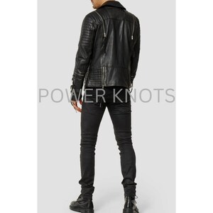 May include: Black leather jacket with zipper details and a quilted pattern. The jacket has a stand-up collar and a zipper closure. The model is wearing black jeans and black boots.