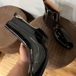 May include: A pair of black patent leather boots with a pointed toe and a zipper up the back. The boots have a gold zipper pull.