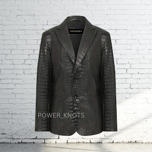May include: A black leather blazer with a crocodile skin texture. The blazer has a notched lapel, two front pockets, and a two-button closure. The text "POWER_KNOTS" is visible at the bottom of the blazer.