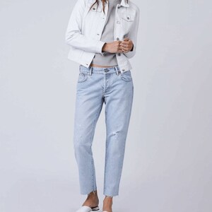 May include: A white denim jacket with a light blue denim shirt underneath. The person is wearing light blue distressed jeans and white shoes.