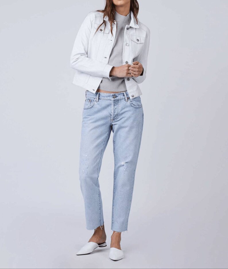 May include: A white denim jacket with a light blue denim shirt underneath. The person is wearing light blue distressed jeans and white shoes.