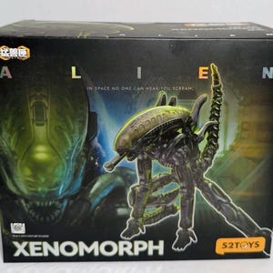 Può includere: Una scatola rettangolare nera per un action figure Xenomorph di 52Toys. La parte anteriore presenta una grande grafica della creatura, il testo ALIEN, la frase IN SPACE NO ONE CAN HEAR YOU SCREAM e la parola XENOMORPH in lettere bianche.