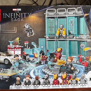 Peut inclure: Une boîte de jeu de construction LEGO The Infinity Saga Iron Man Armory, modèle 76216, comprenant 496 pièces. L'illustration montre un laboratoire à plusieurs niveaux avec diverses armures Iron Man, des figurines dont Tony Stark et Thanos.