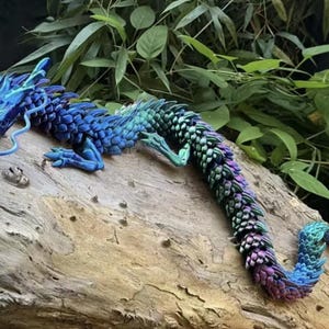 Puede incluir: Una detallada figura articulada de dragón en tonos azules, verdes y morados, posada sobre un tronco de madera desgastado. Las escamas y rasgos del dragón están intrincadamente diseñados, con una larga cola fluida.