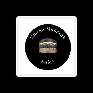Puede incluir: Adhesivo cuadrado con un círculo negro que presenta la Kaaba, un edificio en forma de cubo, con detalles dorados y una base blanca y beige. Las palabras "Umrah Mubarak" están arqueadas sobre la Kaaba, y "NAME" debajo.