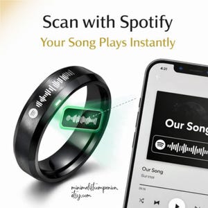 Könnte beinhalten: Schwarzer Smartring mit Spotify-Logo und grün leuchtender Grafik. Der Ring ist mit einem Smartphone verbunden, das einen Song anzeigt. Der Text auf dem Bild lautet "Scan with Spotify, Your Song Plays Instantly."