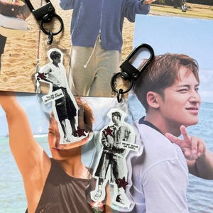 May include: Two clear acrylic keychains with black metal clasps. Each keychain features a black and white graphic of a person with a red star accent. One keychain has the text "You're my favorite muse" and the other says "never leave me lonely."
