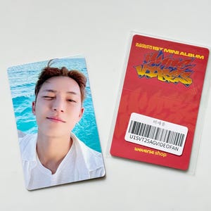 Puede incluir: Una tarjeta fotográfica con una persona en camisa blanca frente al mar azul. Al lado, una tarjeta roja con texto amarillo "S.COUPS 1ST MINI ALBUM" y "HAZARDS". La tarjeta incluye un código de barras y "weverse shop".