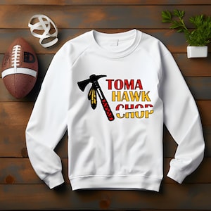 Puede incluir: Sudadera blanca con un gráfico de hacha de guerra roja, amarilla y negra y el texto "Tomahawk Chop".