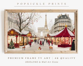May include: Framed print of a winter scene in Paris, featuring the Eiffel Tower and Arc de Triomphe. The artwork depicts a Christmas market with red and gold stalls, snow-covered trees, and figures in winter attire. The text "POPSICLE PRINTS" is at the top.