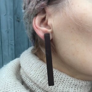 Peut inclure: Une paire de longues boucles d'oreilles rectangulaires brun foncé. Les boucles d'oreilles sont en matériau lisse et mat.