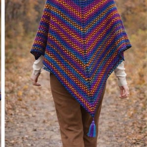 May include: A colorful, handmade crochet poncho in shades of blue, purple, orange, and yellow. The poncho has a geometric pattern and a tassel at the point. The person is wearing a white turtleneck and brown pants.