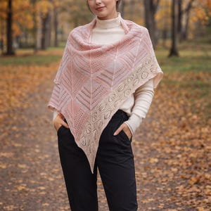May include: A triangular knit shawl featuring a gradient of soft pink and cream colors. The shawl displays a textured geometric pattern throughout the center, finished with a delicate, openwork lace border along the edges in a light cream tone.