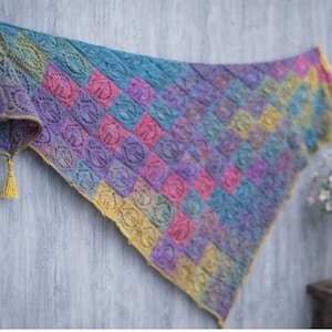 May include: A triangular shawl constructed from a grid of multicolored crochet squares featuring a repeating circular lace pattern. The shawl displays a gradient of blue, purple, pink, and yellow hues, finished with yellow tassels at the corners.