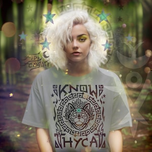 May include: A light green t-shirt with a black graphic design featuring a cat's face, an eye, and the words "KNOW WHY CAT". The image has a forest background with bokeh effects and stars.