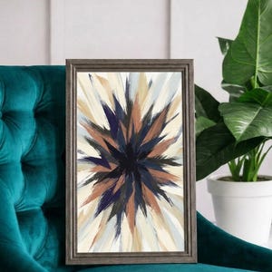May include: A rectangular framed wall art piece featuring an abstract starburst pattern with radiating brushstrokes in shades of deep navy blue, warm brown, cream, and light gray, enclosed in a textured dark gray wooden frame.