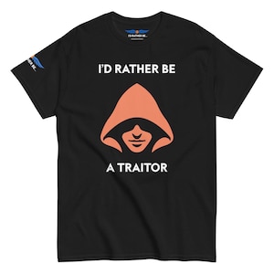 May include: Black t-shirt with the text "I'D RATHER BE A TRAITOR" in white. The shirt features an orange hooded figure graphic. The upper left sleeve has a blue and white graphic. The shirt is made of a soft material.