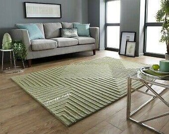 May include: A light green area rug with a geometric pattern. The rug has a square shape with a diamond pattern in the center. The rug is in a living room setting with a gray sofa and a glass end table.