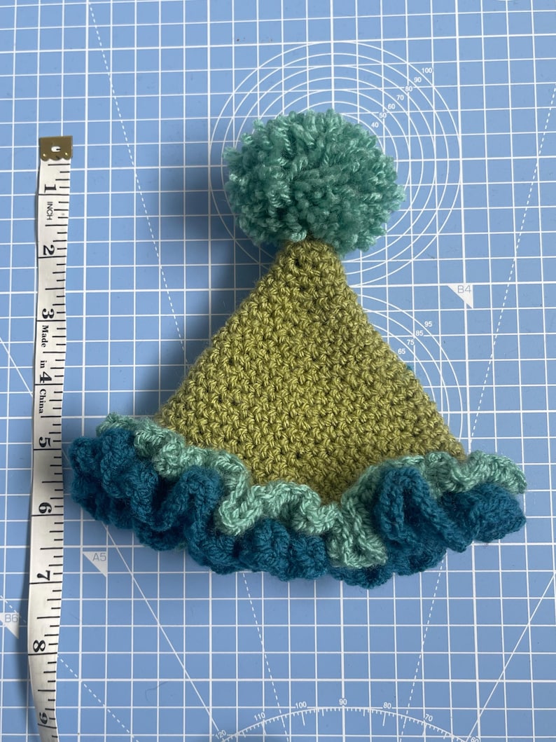 May include: A green crocheted hat with a blue and green ruffled brim and a green pom-pom on top.