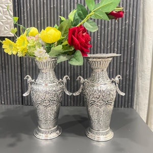 May include: Two silver vases with intricate floral designs and bird-shaped handles, filled with red and yellow flowers.