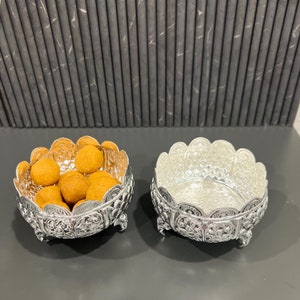 May include: Two silver bowls with intricate floral designs. One bowl is filled with small, round, orange-brown treats.