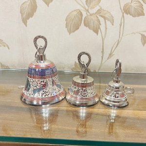 Könnte beinhalten: Drei silberne Glocken mit aufwendigen Designs und bunten Akzenten. Die Glocken sind unterschiedlich groß und in einer Reihe von der größten zur kleinsten angeordnet.