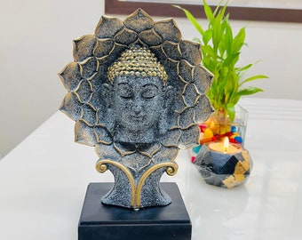 May include: A black and gold Buddha statue with closed eyes, sitting on a black base. The statue is surrounded by a lotus flower design.