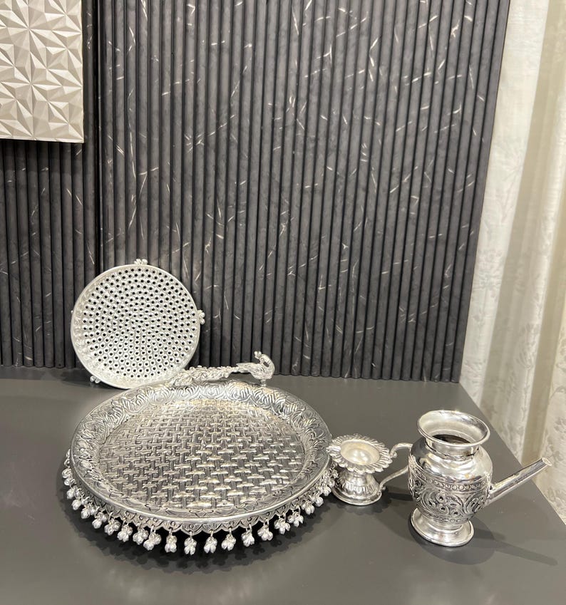 May include: A silver serving tray with a peacock design handle, a small silver bowl, a silver plate with a woven pattern, and a silver jug with a floral design.