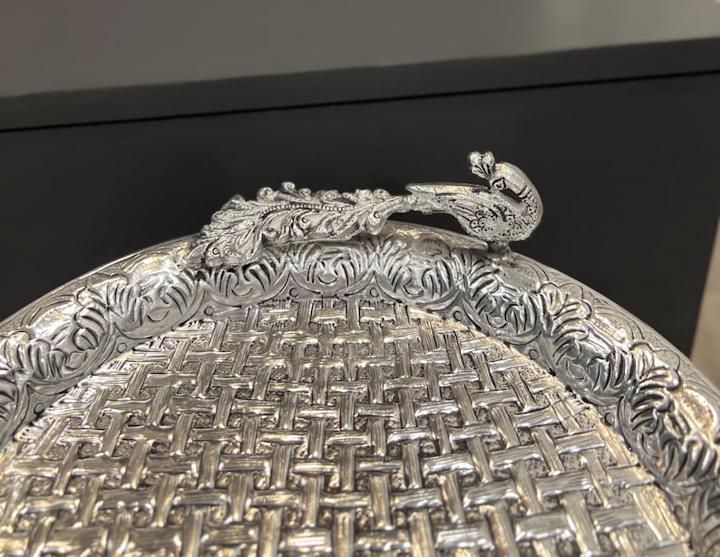 May include: A silver serving tray with an intricate woven pattern and a peacock design handle.