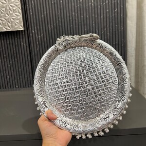 May include: A silver decorative tray with a woven pattern and a peacock design handle. The tray has a beaded edge.