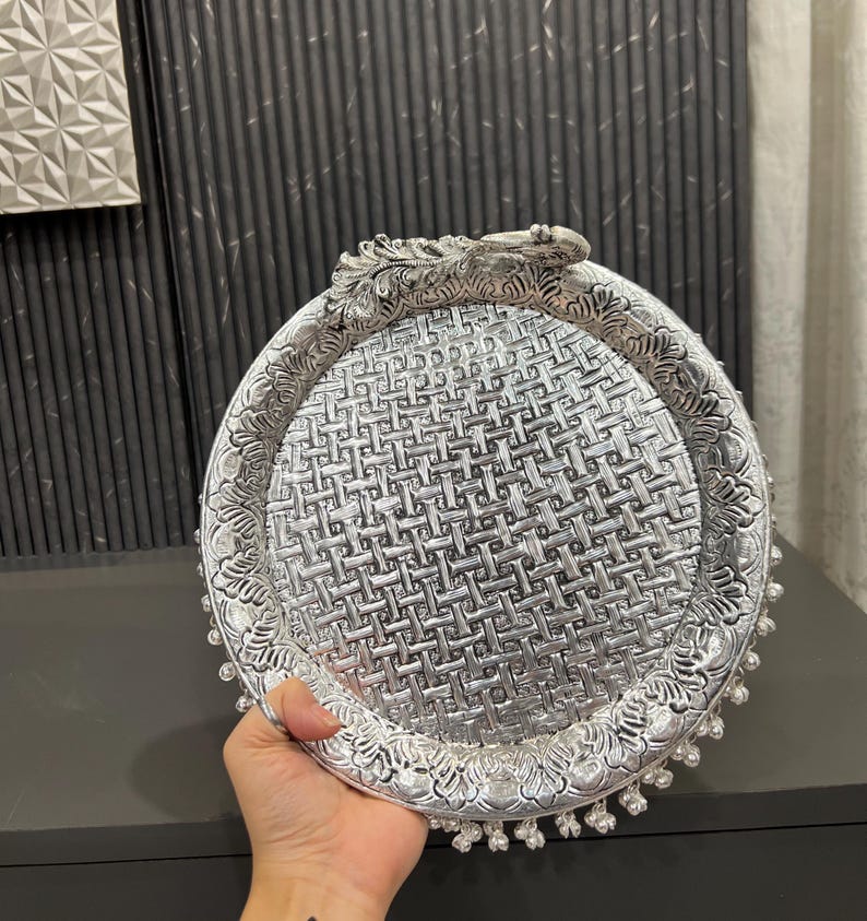 May include: A silver decorative tray with a woven pattern and a peacock design handle. The tray has a beaded edge.