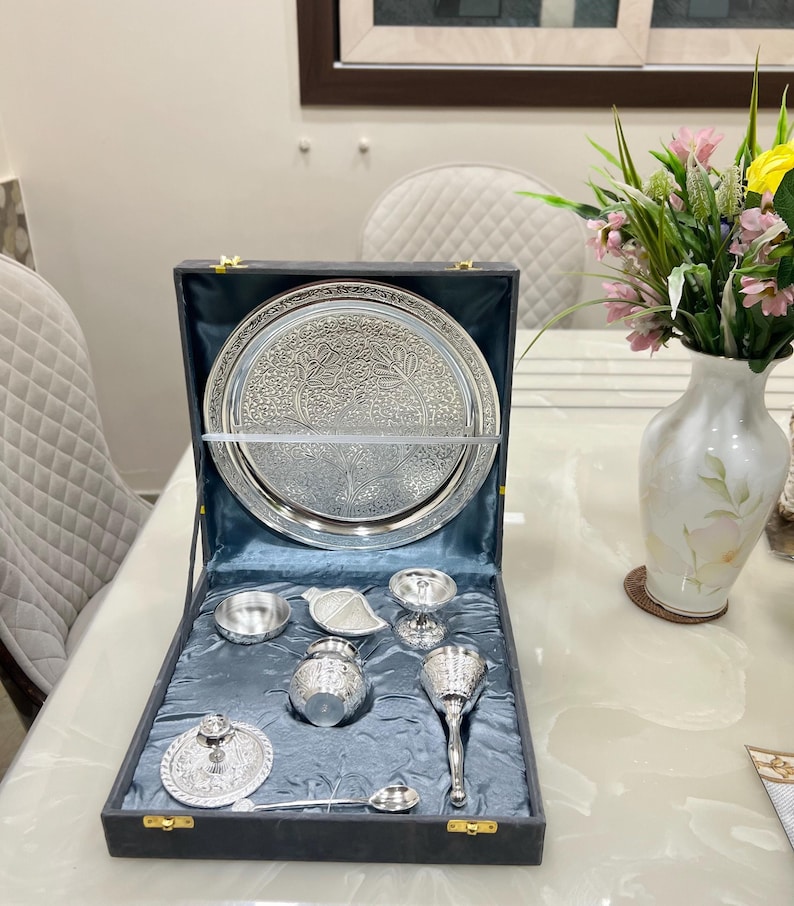 May include: A silver serving set in a blue velvet box. The set includes a large tray, a small bowl, a pitcher, a cup, a spoon, and a lid. The set is perfect for serving tea or coffee.