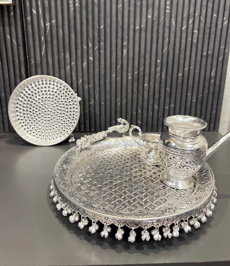 May include: A silver tray with intricate designs and a beaded border. The tray is filled with various silver items, including a pitcher, a small bowl, and a ladle.