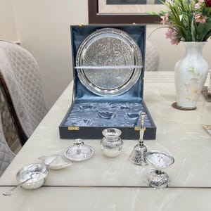 May include: A silver serving set with a tray, a small pot, a bell, and two bowls. The set is in a black box with a blue velvet lining.