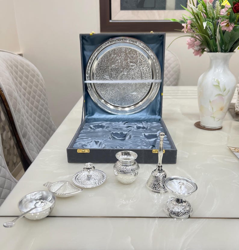 May include: A silver serving set with a tray, a small pot, a bell, and two bowls. The set is in a black box with a blue velvet lining.