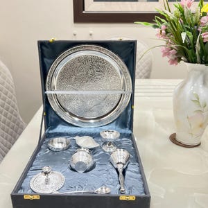 May include: A silver serving set in a black velvet box. The set includes a large plate, a small bowl, a spoon, a small cup, and a small pitcher.