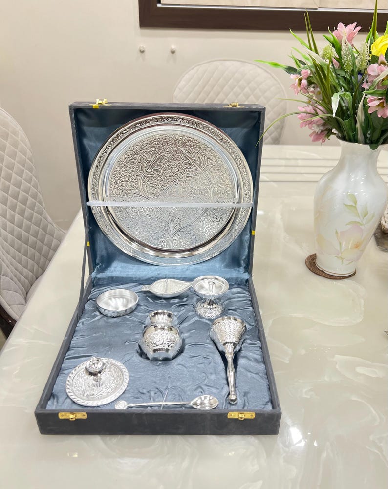 May include: A silver serving set in a black velvet box. The set includes a large round tray, a small bowl, a pitcher, a spoon, a small cup, and a small lidded dish. The tray and all the pieces have intricate floral designs.