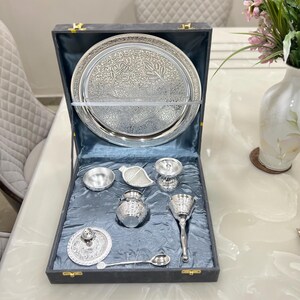May include: A silver serving set in a black velvet lined box. The set includes a large round tray, a small bowl, a sugar bowl, a creamer, a pitcher, a spoon, and a lidded dish.