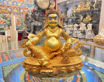 May include: A gold-colored statue of a deity with a round belly, sitting in a lotus position. The statue is adorned with intricate details and has a blue and white face.