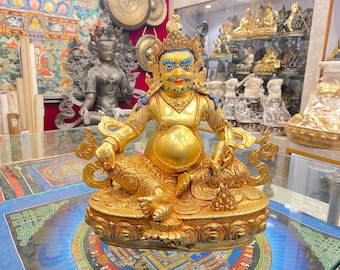 May include: A golden statue of a deity with a round, full belly, sitting in a meditative pose. The statue is adorned with intricate details and has a blue and gold color scheme.