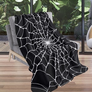 May include: Black and white throw blanket with a spiderweb design. The blanket is draped over a chair in a modern living room.